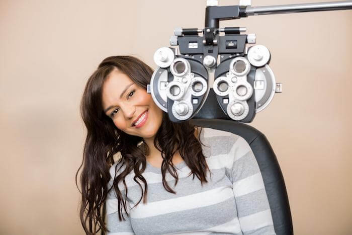 Happy woman sitting behind a phoropter during an eye exam